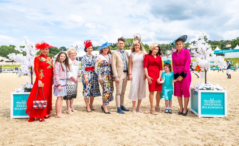 A group of people dressed in vibrant and sophisticated clothing, including blue, red, and pink outfits, with fabulous hats, celebrating Ladies Day at Bolesworth International.