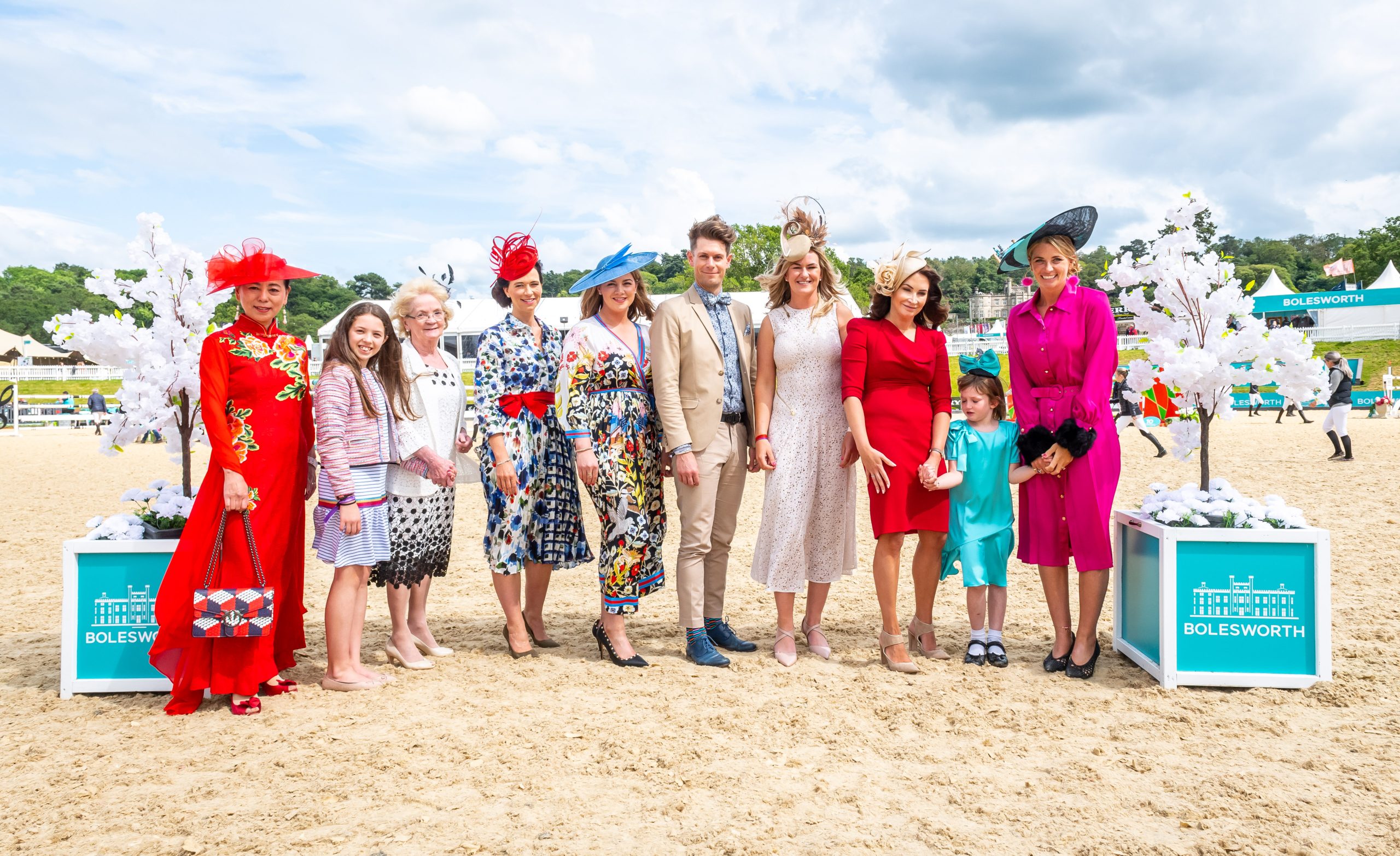 A group of people dressed in vibrant and sophisticated clothing, including blue, red, and pink outfits, with fabulous hats, celebrating Ladies Day at Bolesworth International.