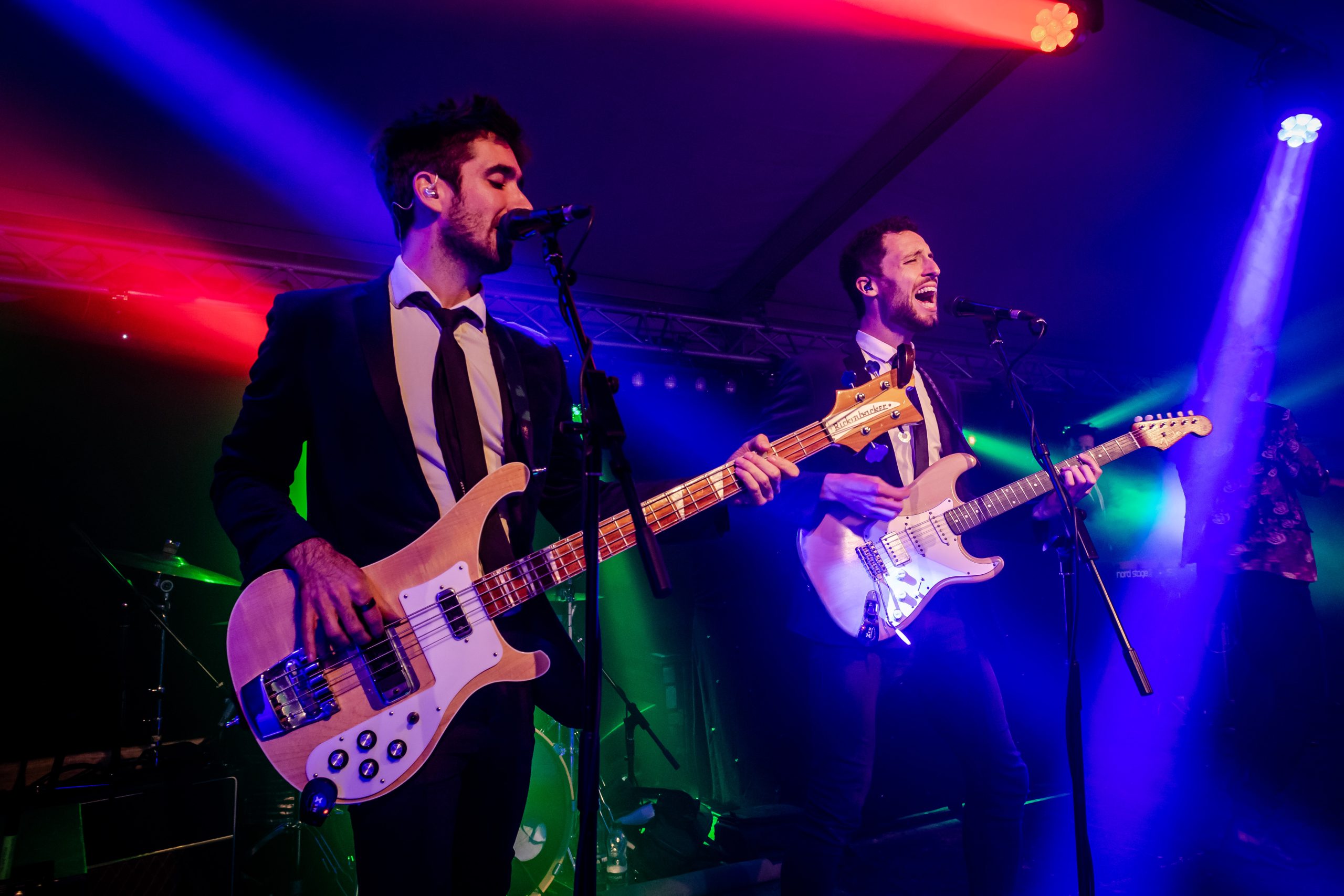 A live band performing at Bolesworth International Horse Show’s nightlife event, featuring two musicians in black suits playing guitars under vibrant stage lighting.
