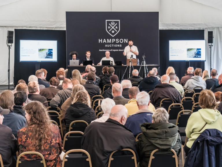 Conference hosted by Hampson Cars, featuring a professional speaker addressing an audience in a well-lit venue with branded elements.