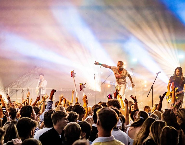 Excited crowd at a live concert with vibrant stage lights and performers engaging the audience.