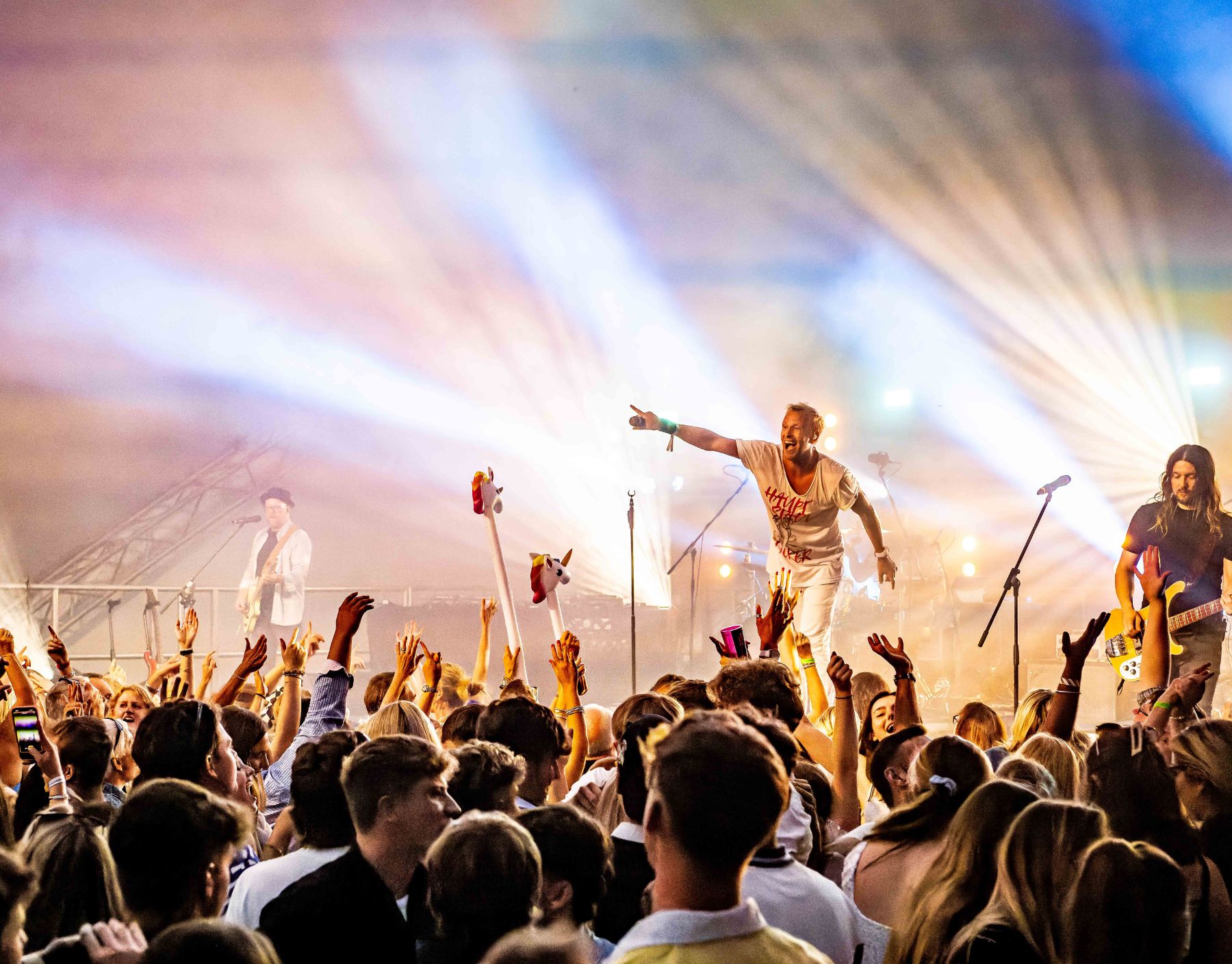 Excited crowd at a live concert with vibrant stage lights and performers engaging the audience.